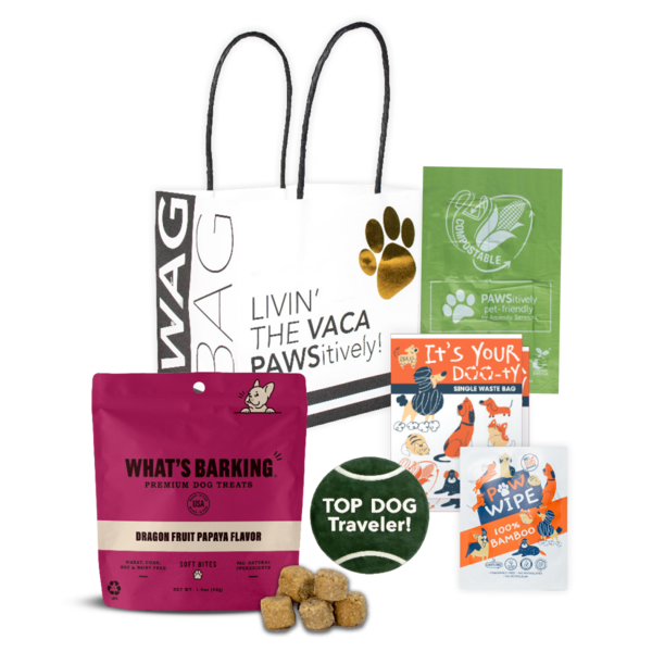 WAG Bag pet gift set including What's Barking dog treats, waste bags, a paw wipe, and a tennis ball, displayed with a white tote bag