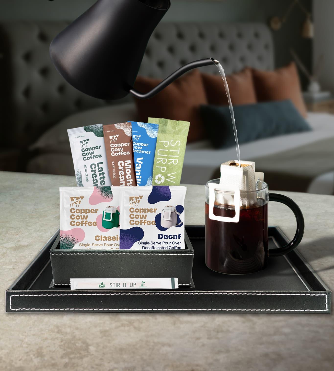 Copper Cow Coffee pour-over setup with assorted creamer packets and glass mug on hotel room tray